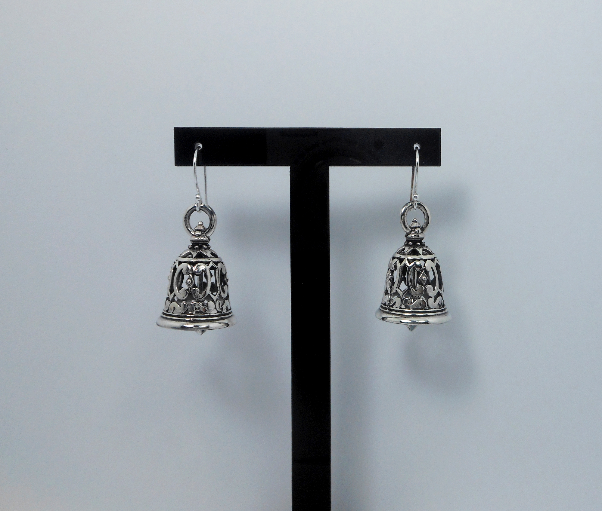 A pair of handcrafted 925 sterling silver bell-shaped drop earrings featuring intricate Thai art textured patterns and a high-polished oxidized finish, displayed on a stand.