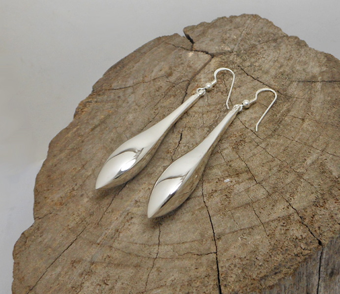 A pair of handcrafted 925 sterling silver elongated puffy teardrop earrings with a high-polished, reflective finish, displayed on a natural wood surface.