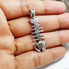 A macro photograph of a polished, handcrafted 925 sterling silver fishbone pendant held in an open palm.