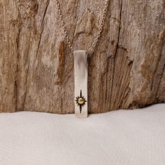 A close-up photograph of a handcrafted 925 sterling silver rectangular bar pendant featuring a textured sun design with a gold accent, displayed against a rustic wood background.
