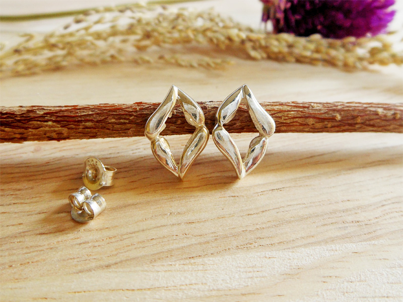 Pair of handmade 925 sterling silver stud earrings with an abstract evil eye shape, resting on a wooden branch.