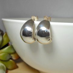 Pair of handmade 925 sterling silver petal-shaped hoop stud earrings with a high-polished mirror finish, resting on the edge of a white bowl with a succulent nearby.