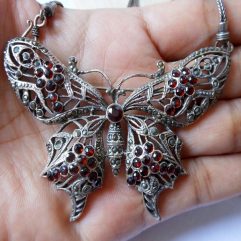 A detailed close-up of a large, handcrafted 925 sterling silver butterfly pendant adorned with intricate marcasite stones and deep red garnet accents, designed to be worn as both a brooch and a necklace set.