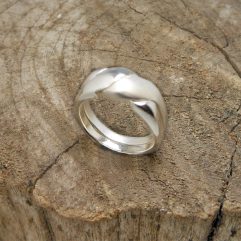 A handcrafted 925 sterling silver double bypass ring featuring an intertwined design, resting on a rustic wood surface.