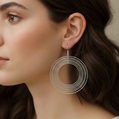 A close-up profile view of a woman wearing large, lightweight 925 sterling silver dangle earrings composed of multiple concentric, smooth, shiny, and spinning circles, referencing