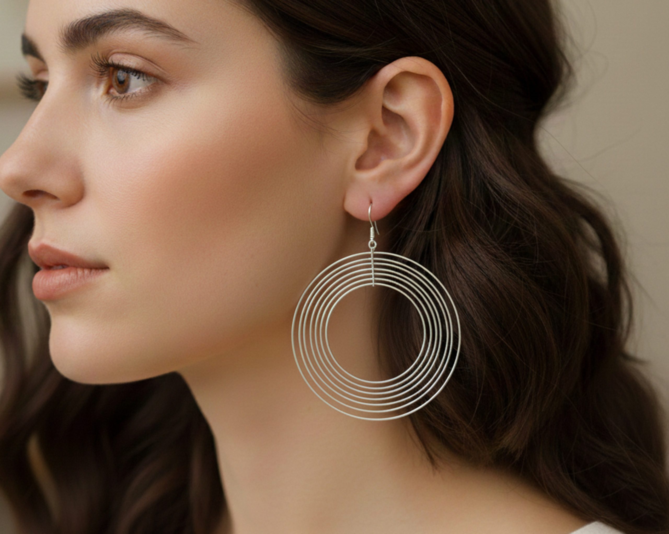 A close-up profile view of a woman wearing large, lightweight 925 sterling silver dangle earrings composed of multiple concentric, smooth, shiny, and spinning circles, referencing