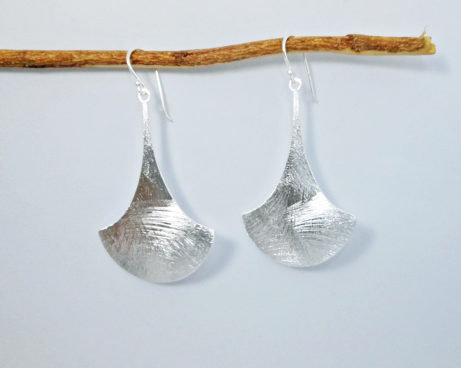 A pair of handcrafted 925 sterling silver sandy textured bell flower drop earrings hanging elegantly from a branch against a clean background.