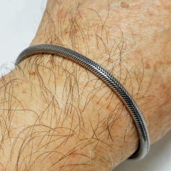 A close-up view of a smooth, flexible round snake chain bracelet with an artisan hook clasp, showcased on a modeled on a wrist.
