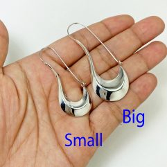 A pair of handcrafted 925 sterling silver puffy pipe dangle hoop earrings held in a hand, showcasing their smooth, high-polished sculptural design, available in two sizes.