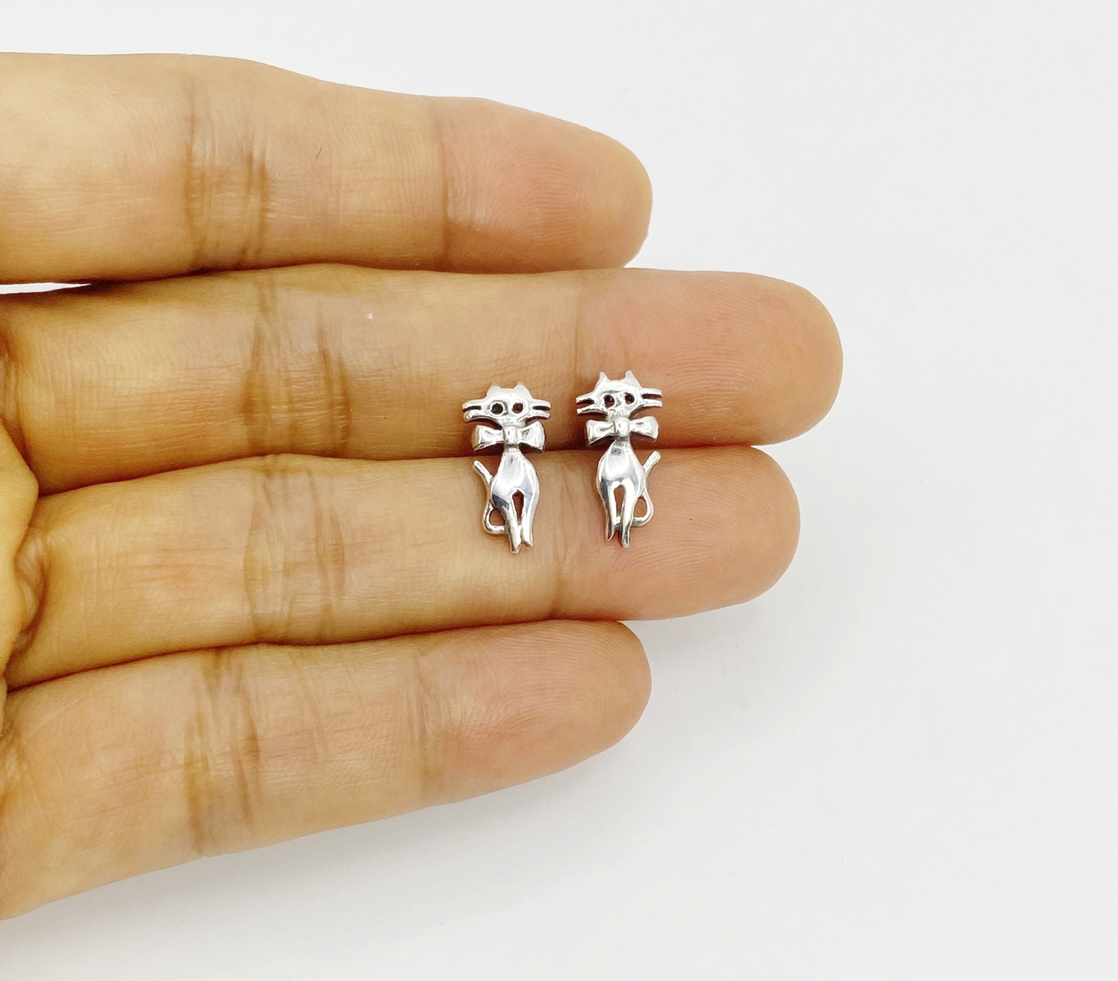 dainty 925 sterling silver cat stud earrings resting on palm for scale.