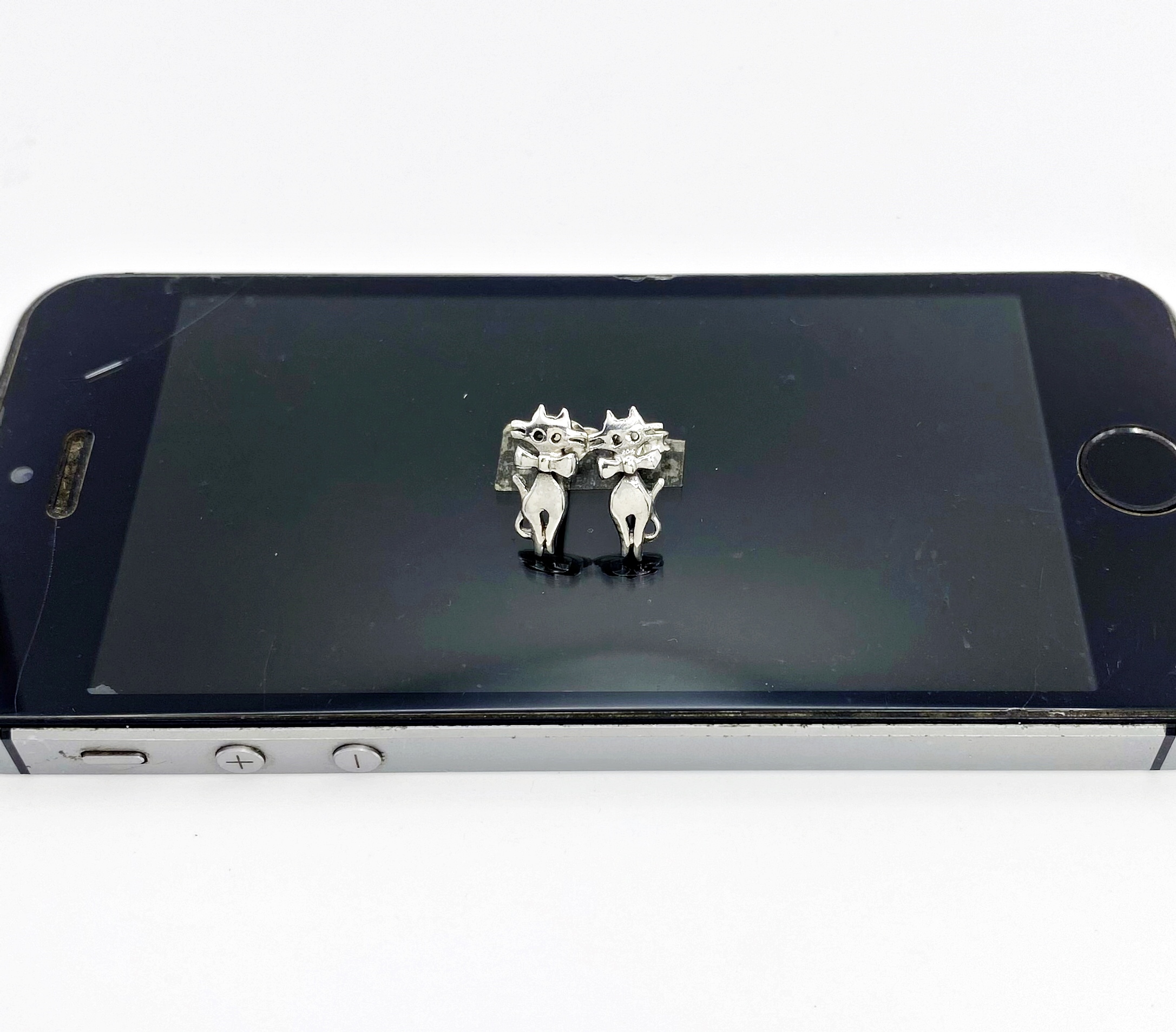 silver cat stud earrings placed on a black smartphone surface.