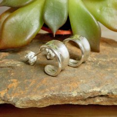 Pair of handmade 925 sterling silver concave hoop stud earrings with a highly polished mirror finish, resting on a stone surface.