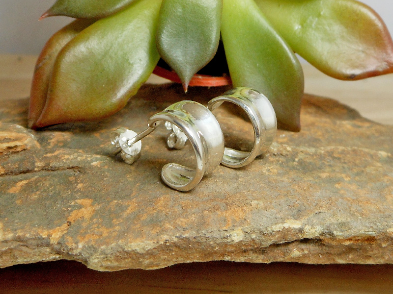 Pair of handmade 925 sterling silver concave hoop stud earrings with a highly polished mirror finish, resting on a stone surface.