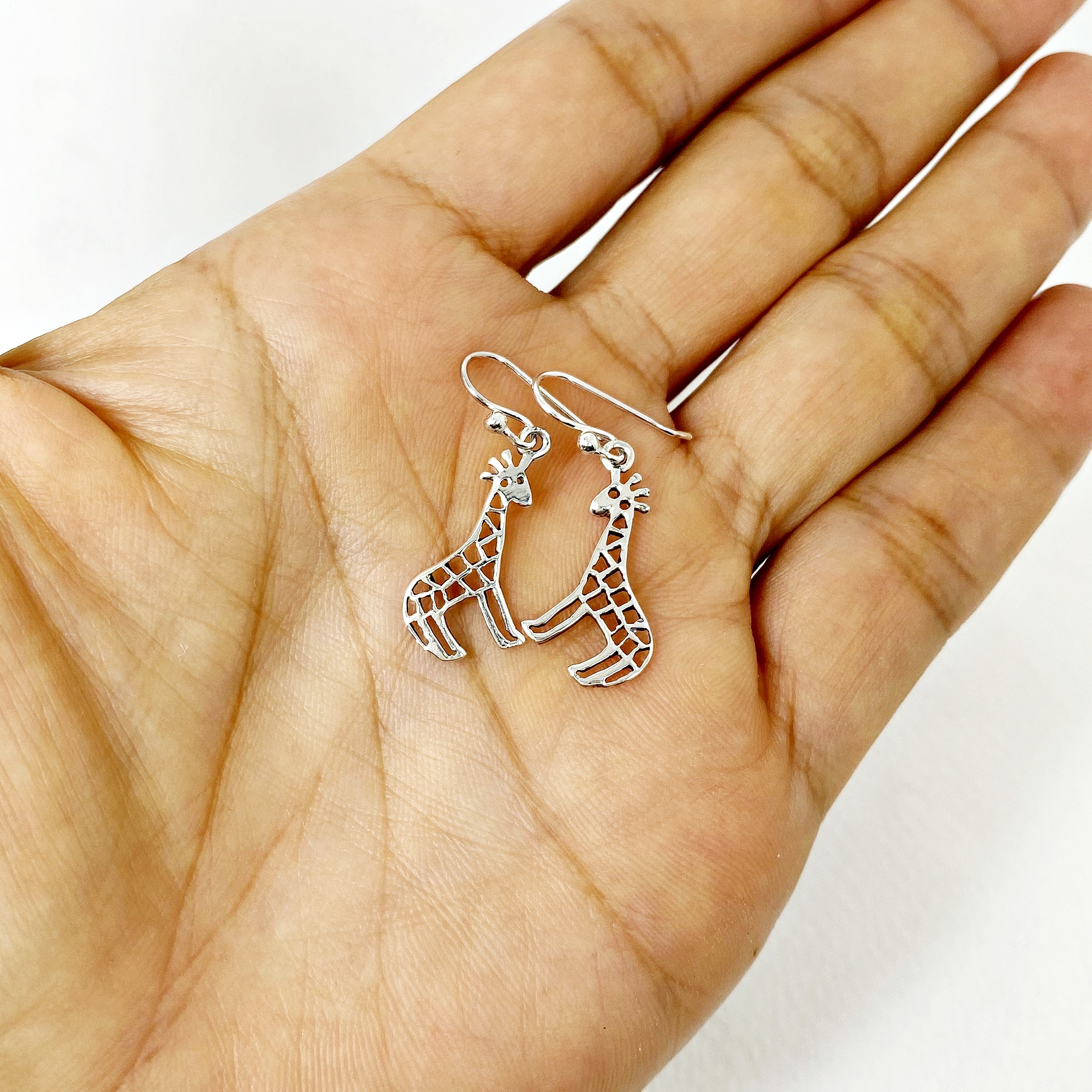 Cutout Giraffe Dangle Earrings resting gently on a hand to show scale.