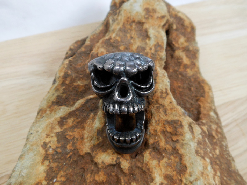 A detailed macro photograph showing a heavy, handcrafted 925 sterling silver skull pendantĀ a model wearing the skull as a statement necklace.