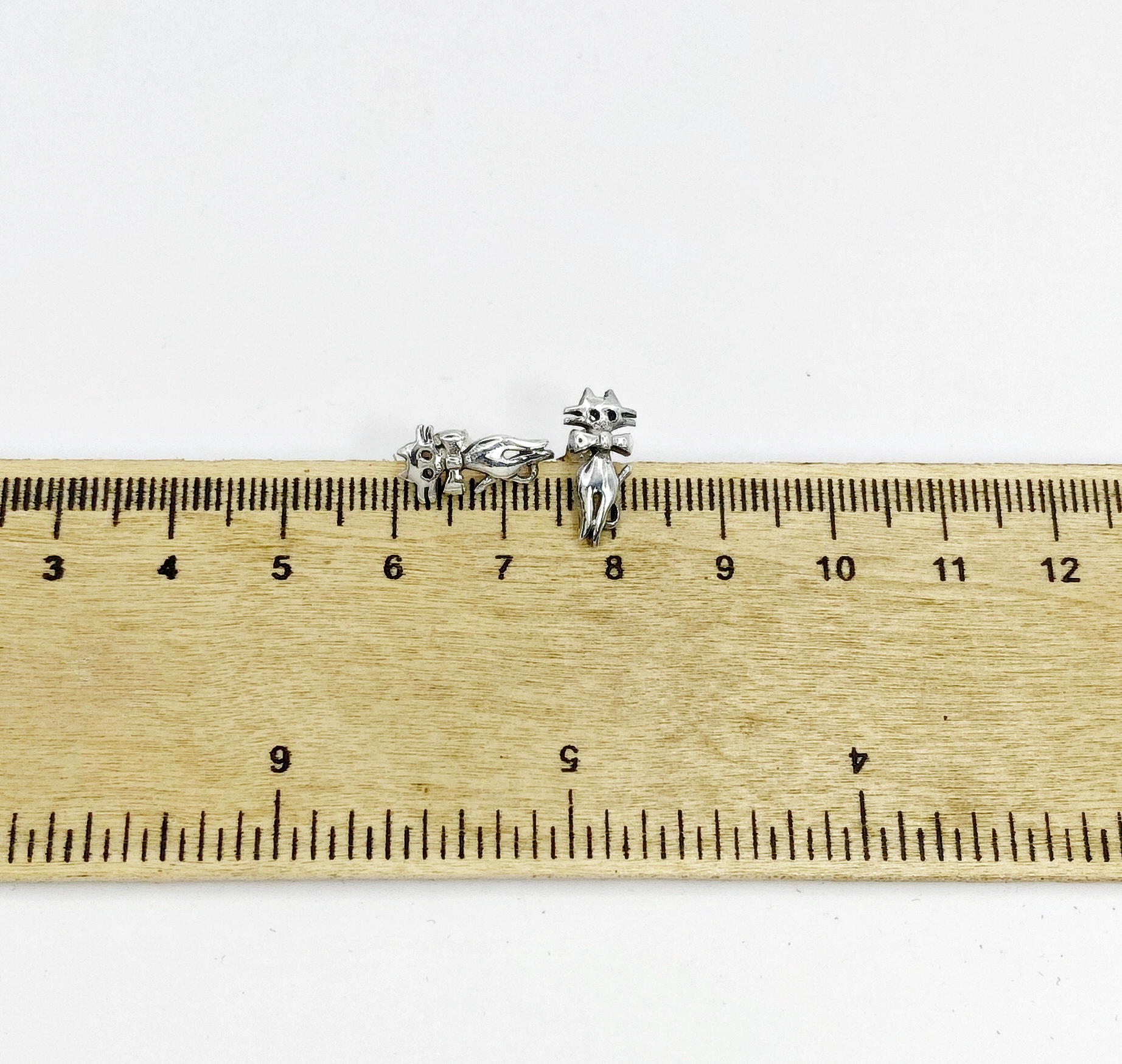 cat stud earrings measured against a wood ruler for sizing.