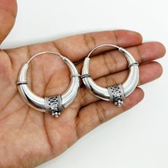 A pair of handcrafted 925 sterling silver hoop earrings featuring a puffy, art deco-inspired tribal design with intricate oxidized wirework, displayed in a hand
