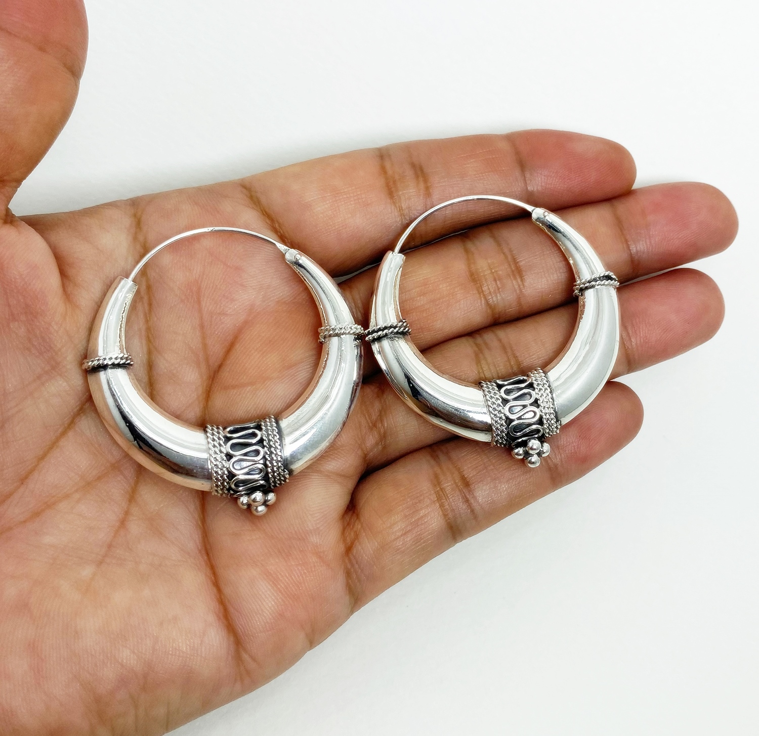 A pair of handcrafted 925 sterling silver hoop earrings featuring a puffy, art deco-inspired tribal design with intricate oxidized wirework, displayed in a hand