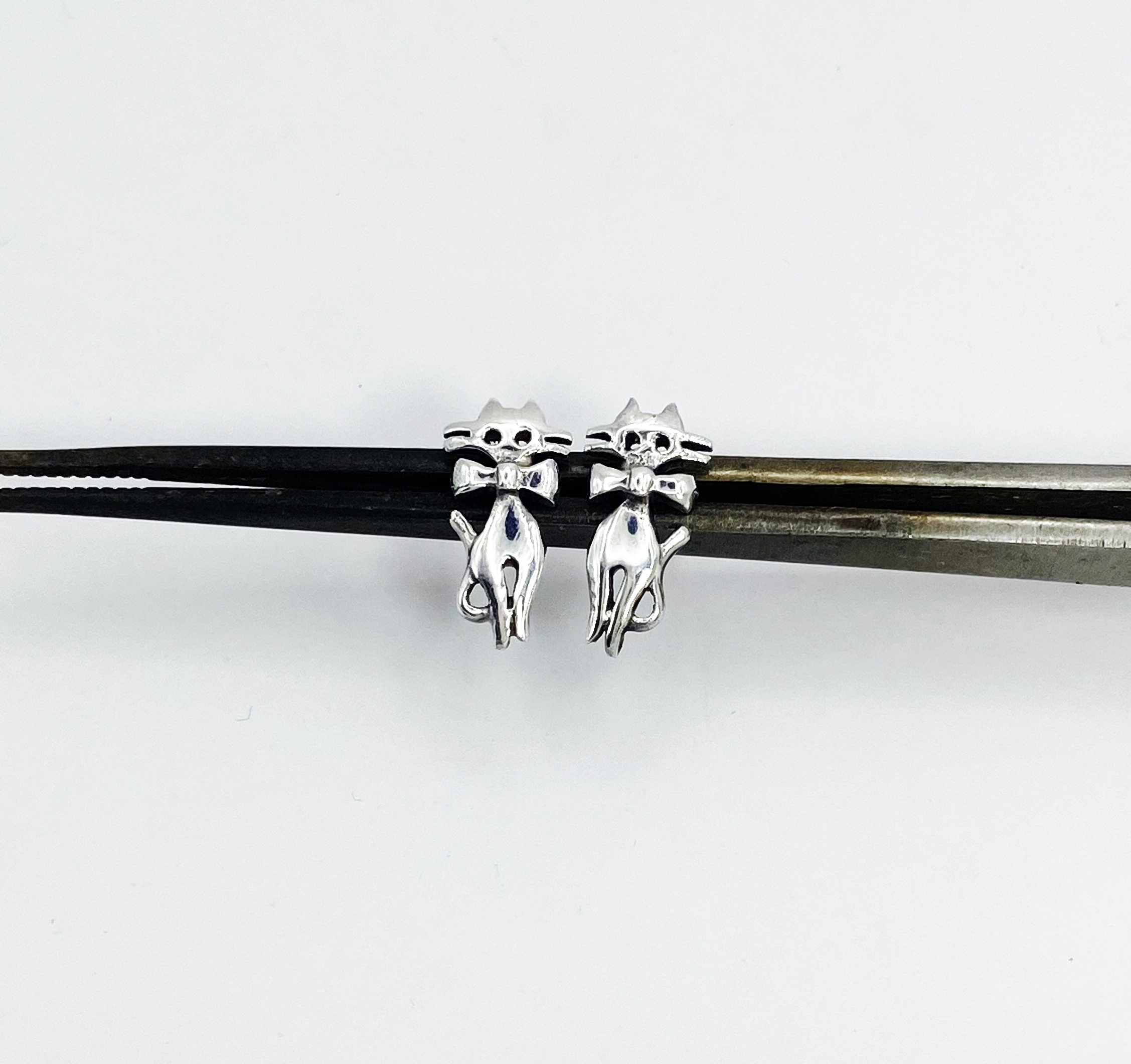 close up of silver cat stud earrings with bow close up.