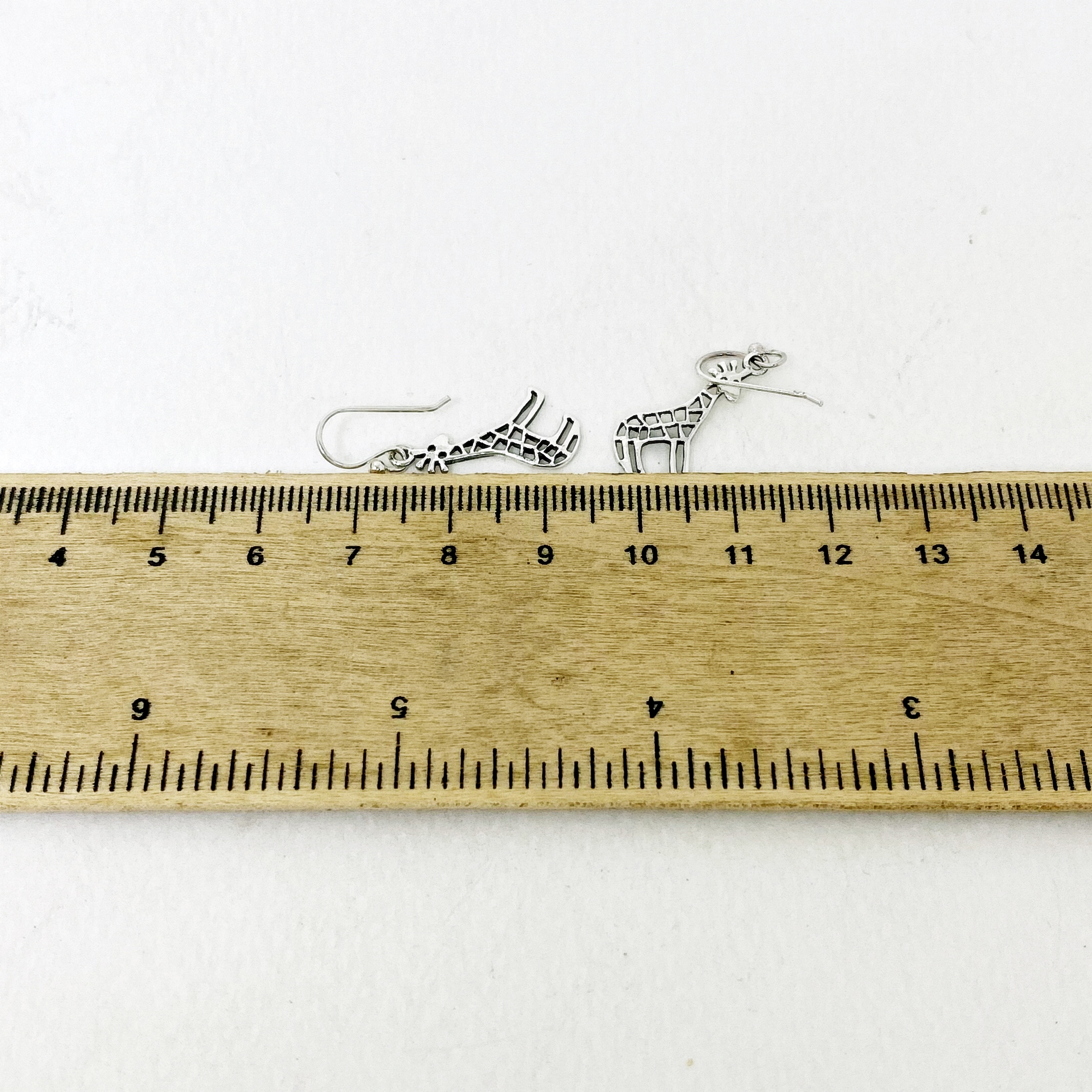 Cutout Giraffe Dangle Earrings placed next to a ruler for dimension reference.