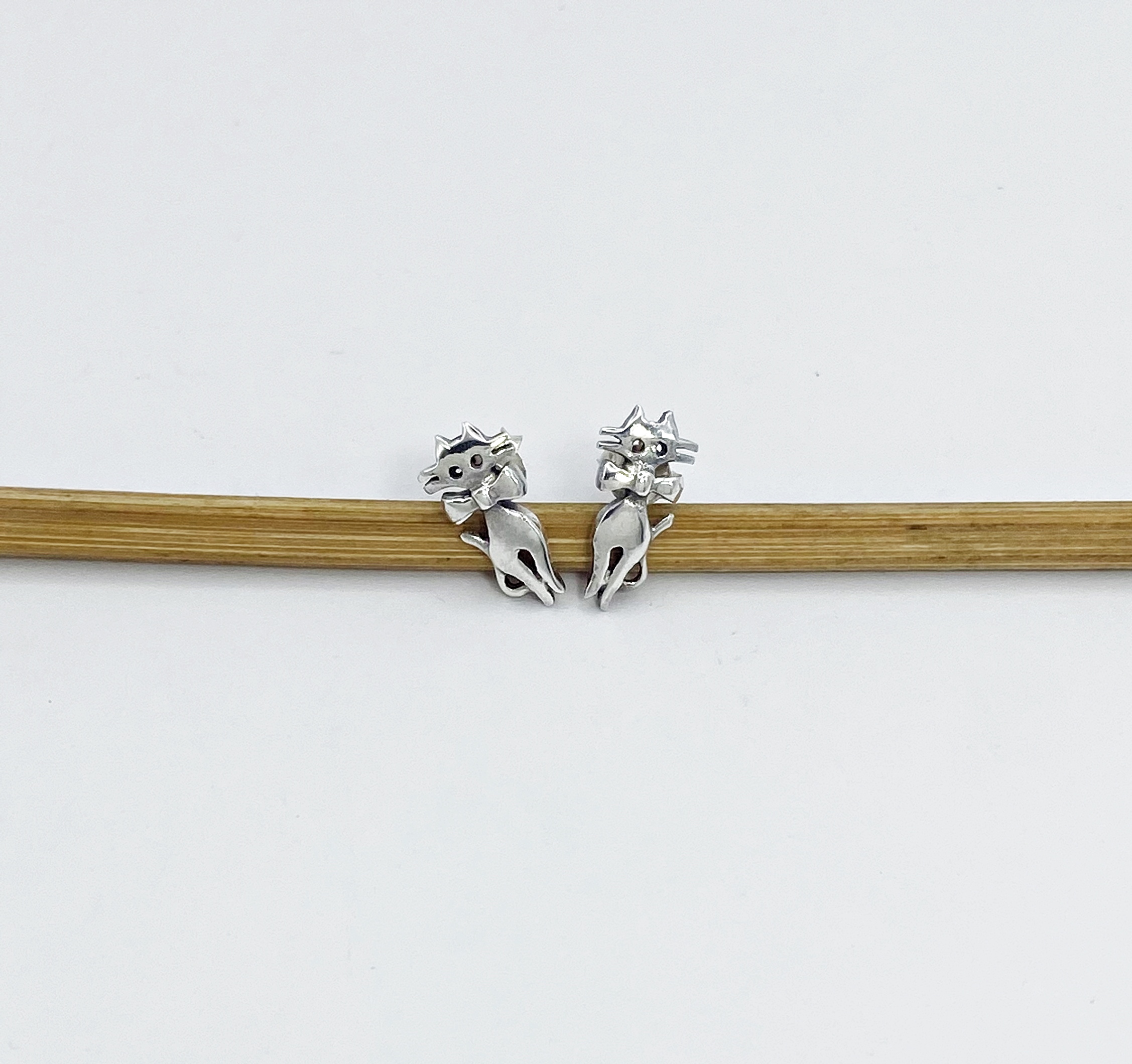 sterling silver cat earrings displayed on wooden stick.