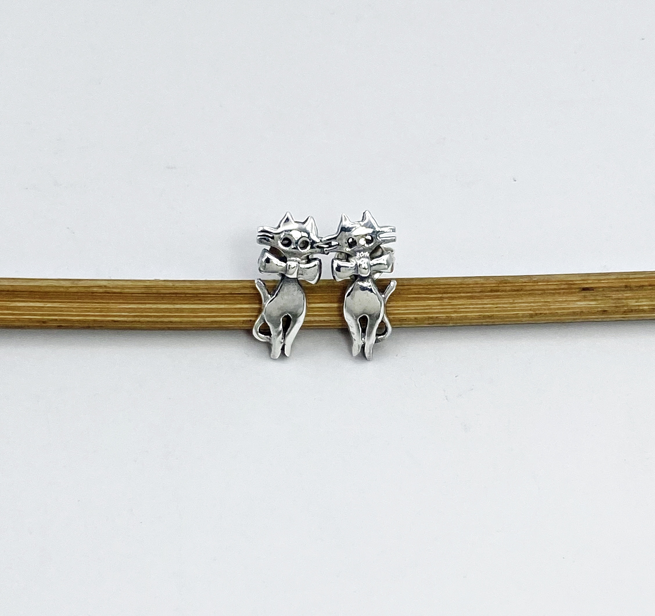 front view of 925 silver cat and bow stud earrings on wooden stick.