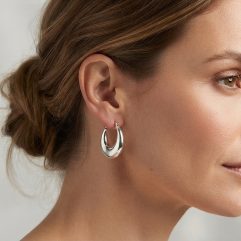 A pair of handcrafted 30mm crescent moon shaped puffy hoop earrings in 925 sterling silver, featuring a smooth, polished finish on model.