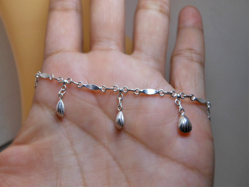 Detailed close-up of the scallop shell charms on the silver anklet
