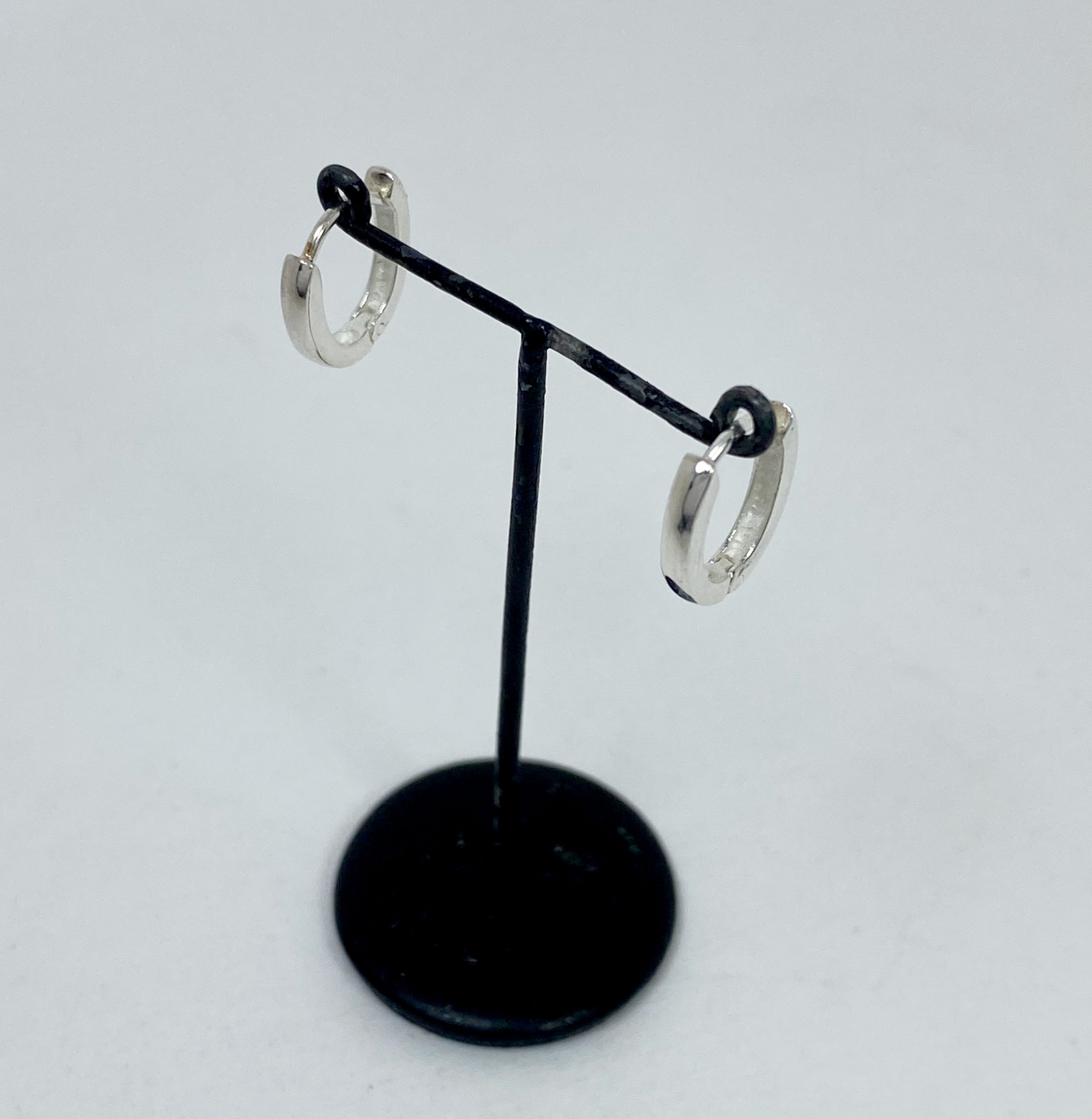 A pair of polished 925 sterling silver oval huggie hoop earrings, 2mm wide, displayed on a small black stand.