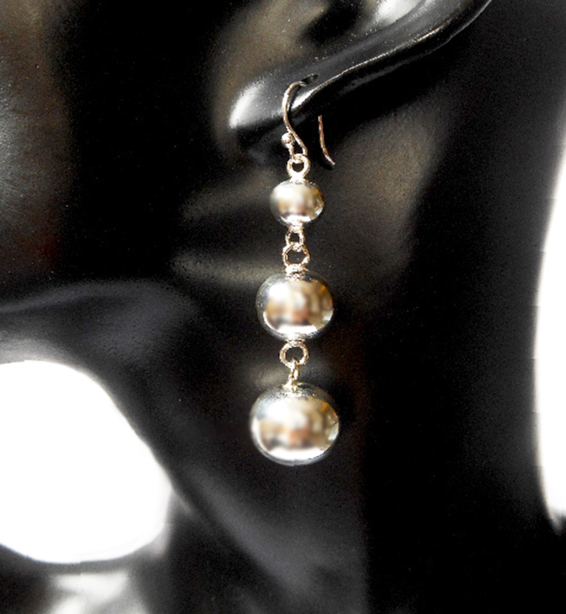 A pair of handcrafted 925 sterling silver triple ball dangle earrings with a tapered, high-polished design worn on a mannequin ear.