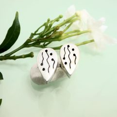 Pair of handmade 925 sterling silver teardrop stud earrings featuring a unique etched wavy line and dot pattern with a puffy, dimensional profile, resting near white flowers.