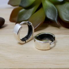 A pair of 925 sterling silver 5mm wide flat round huggie hoop earrings resting on a light wood surface with a succulent in the background.