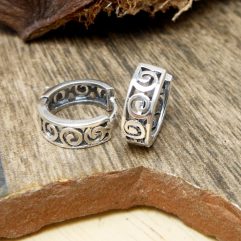 A pair of handcrafted 925 sterling silver huggie hoop earrings with an intricate spiral pattern and oxidized finish, resting on a rustic wooden surface.