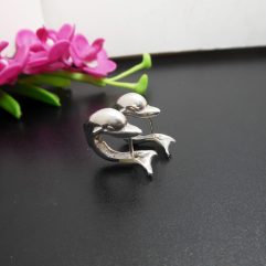 A pair of handcrafted 925 sterling silver dolphin-shaped hug hoop earrings displayed on a dark surface with pink flowers in the background.