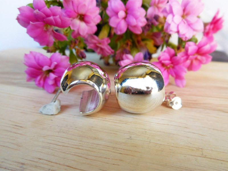 Pair of handmade 925 sterling silver puffy wide hoop earrings shown on a wooden surface with pink flowers.