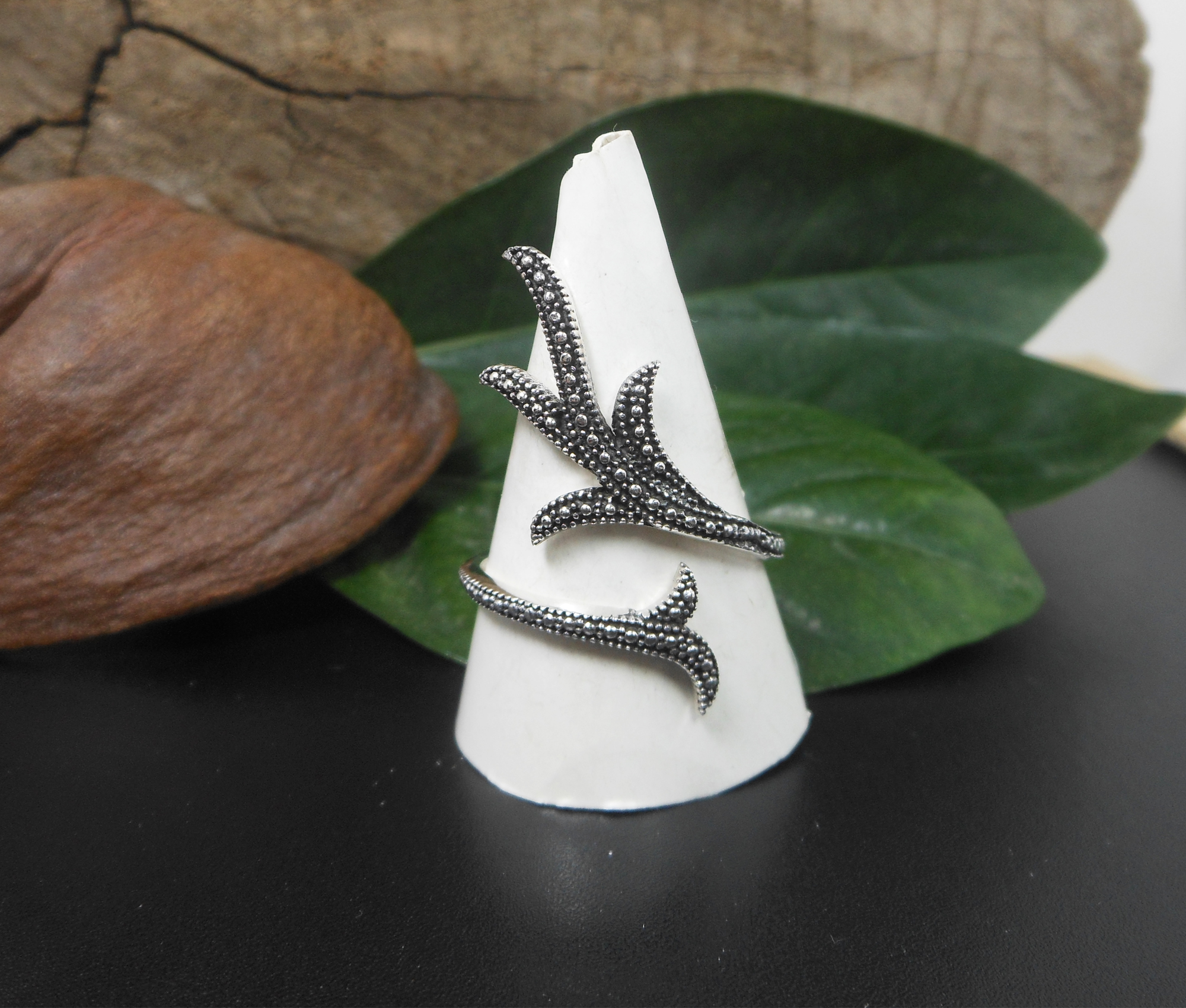 A handcrafted 925 sterling silver ring featuring a detailed, textured leafy branch design in an adjustable wrap-around style, shown on a display cone