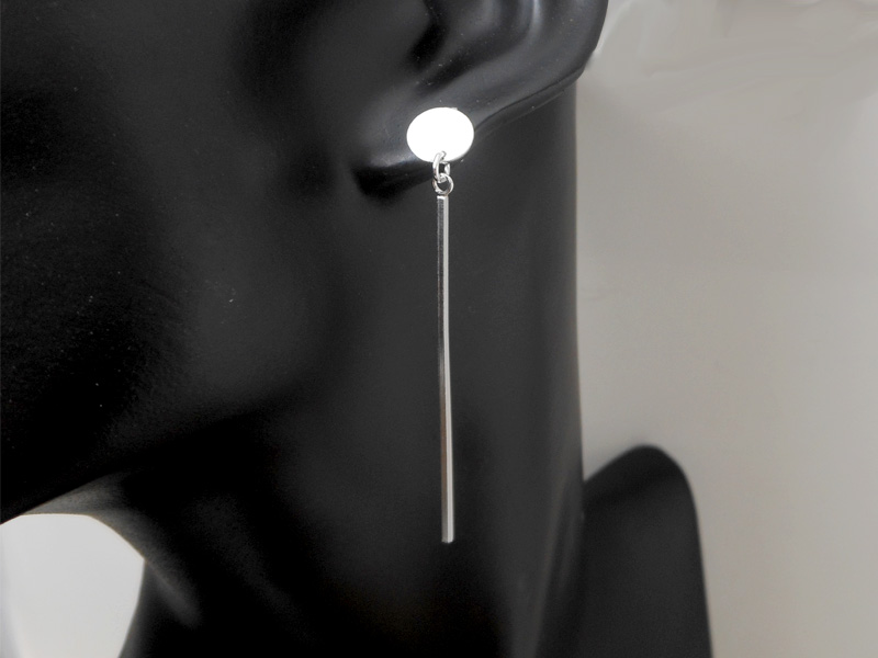 A pair of handcrafted 925 sterling silver minimalist drop earrings, featuring a small disc post connected to a long, thin square bar dangle, worn on a black mannequin ear.