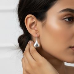 Side profile of a woman with short hair wearing silver puffy teardrop threader earrings.