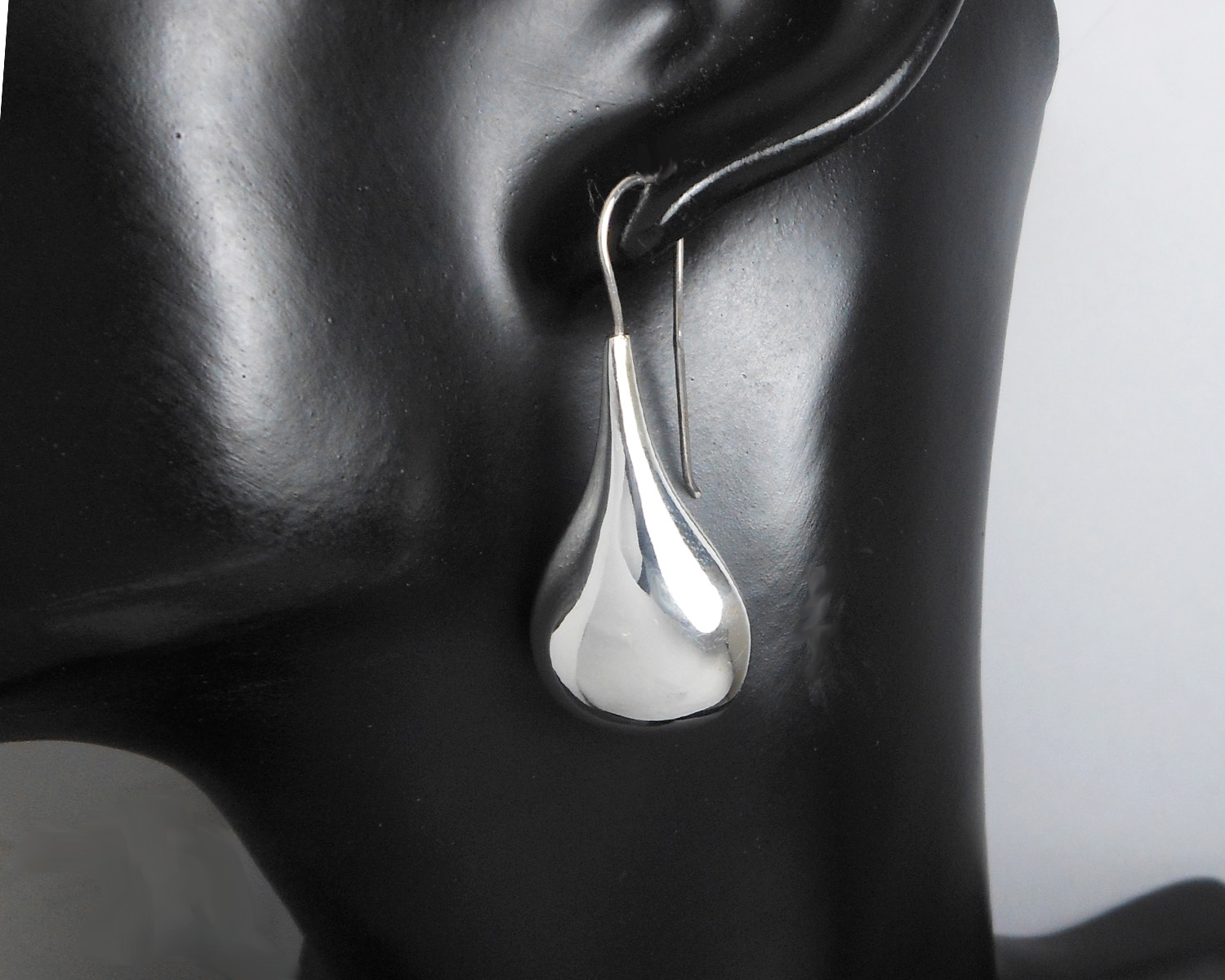 A single silver puffy teardrop earring displayed on a black stand.