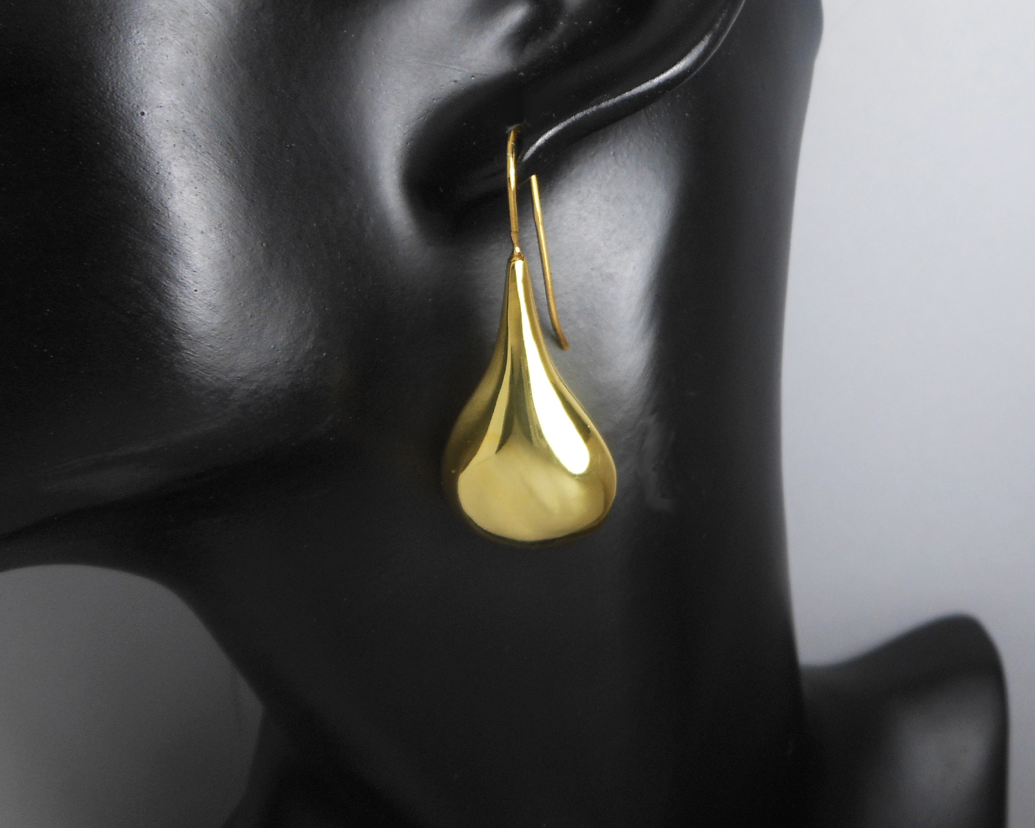 A single gold puffy teardrop earring displayed on a black stand.