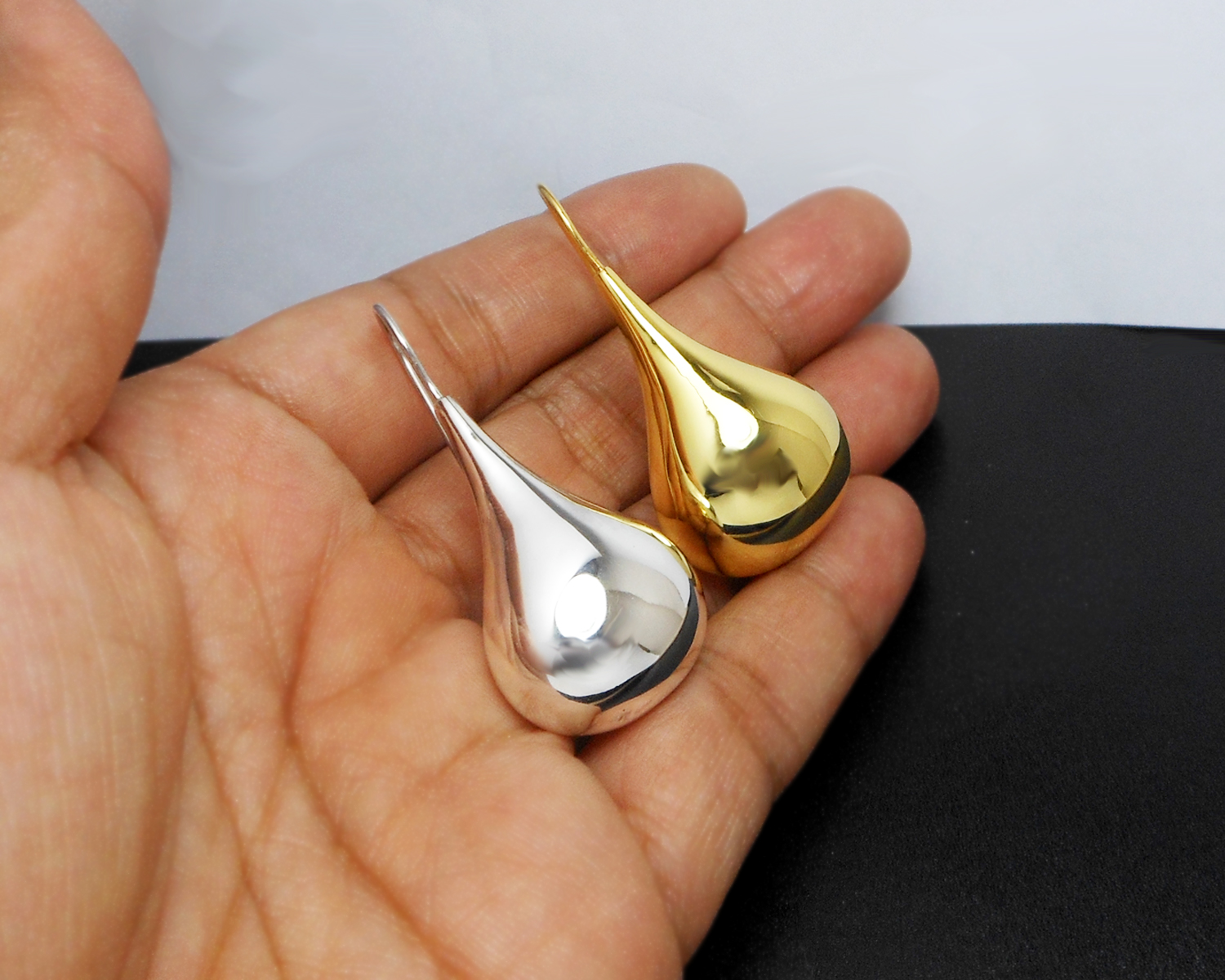 A person's hand holding and comparing silver and gold color puffy teardrop earrings.