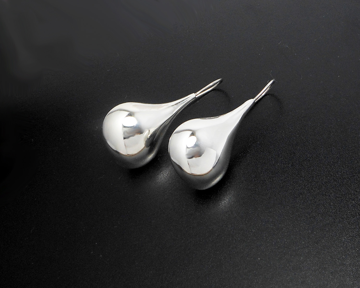 A pair of silver puffy teardrop earrings against a black background.