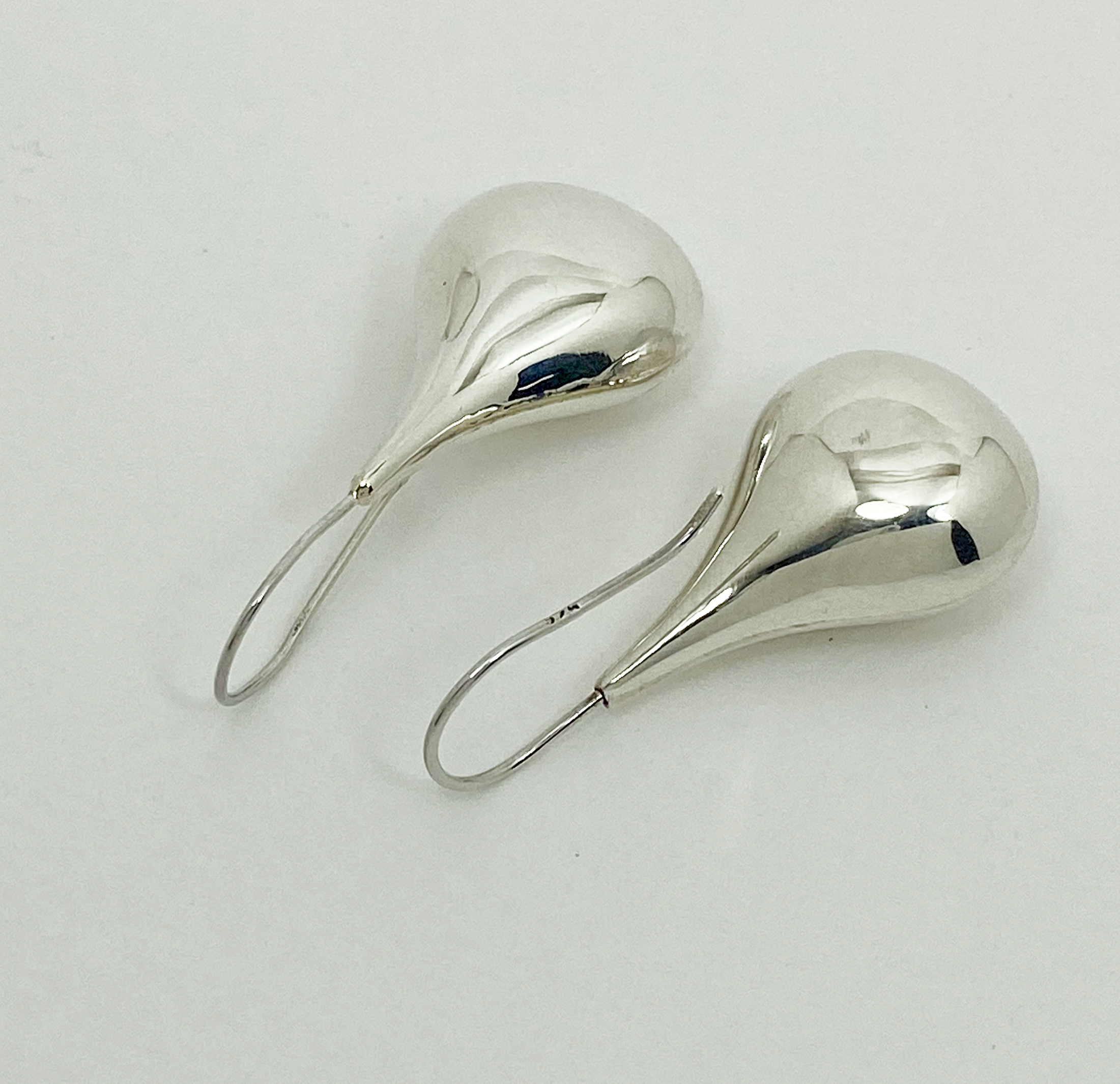 Two silver puffy teardrop earrings lying on a neutral surface.