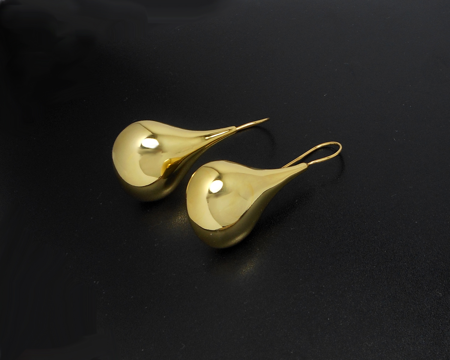 Two gold puffy teardrop earrings lying on a black background.