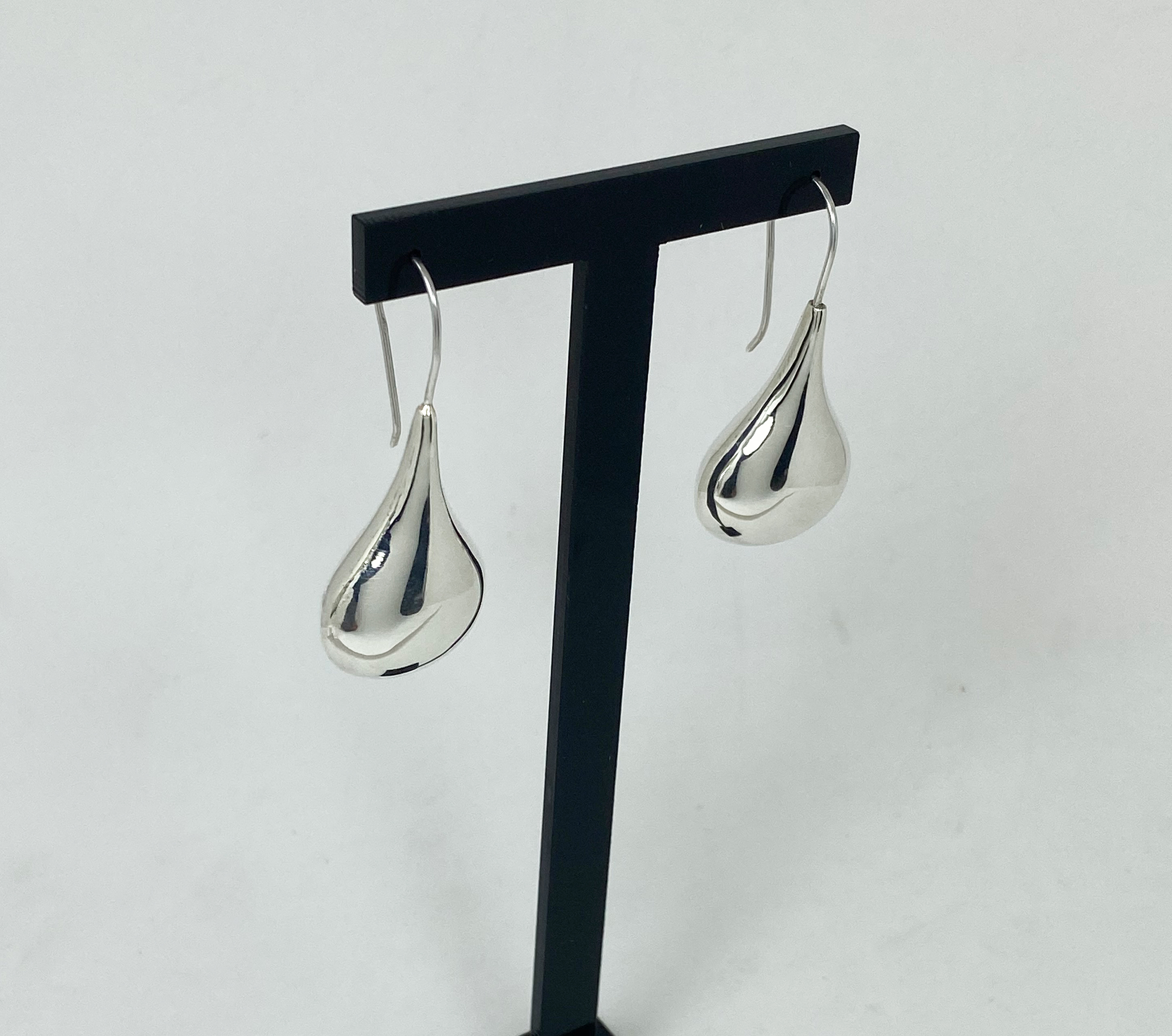A pair of silver puffy teardrop earrings hanging from a jewelry display stand, shown from a left-side angle.