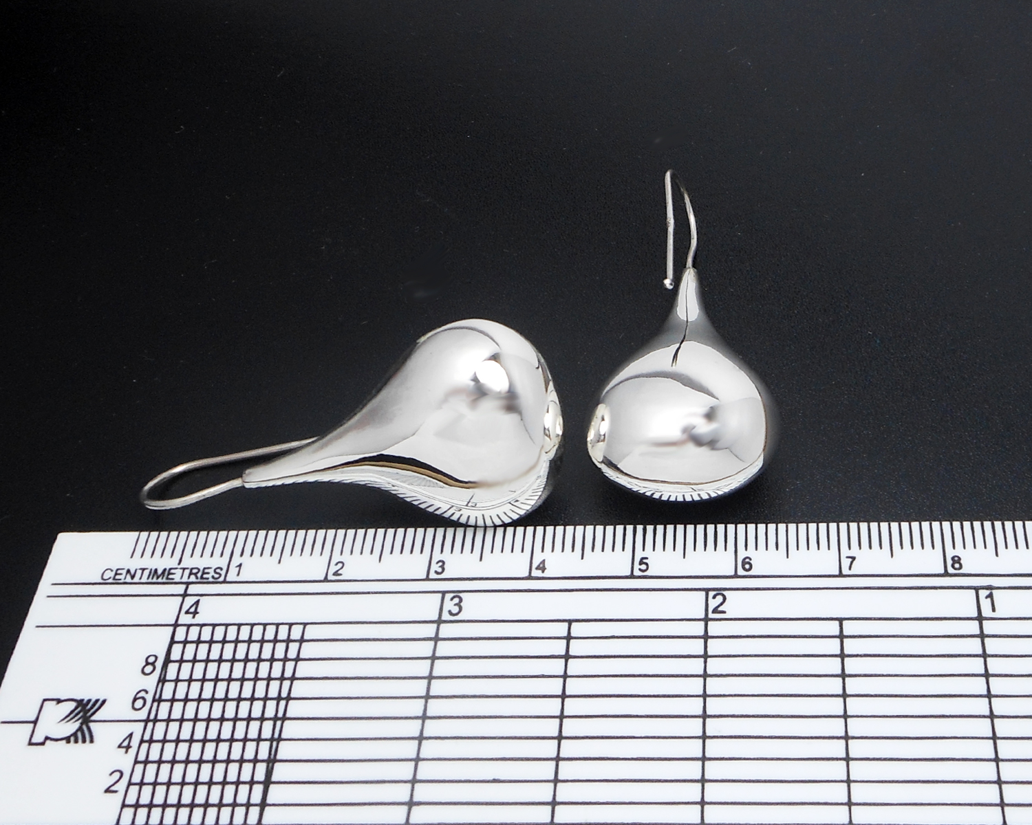 A pair of silver puffy teardrop earrings placed on a measuring tool to show scale.