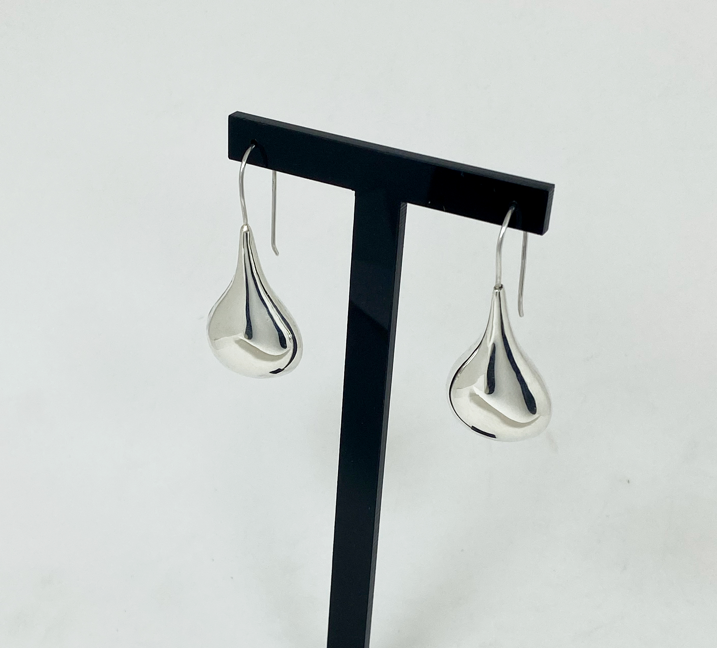 A pair of silver puffy teardrop earrings hanging from a jewelry display stand, shown from a right-side angle.