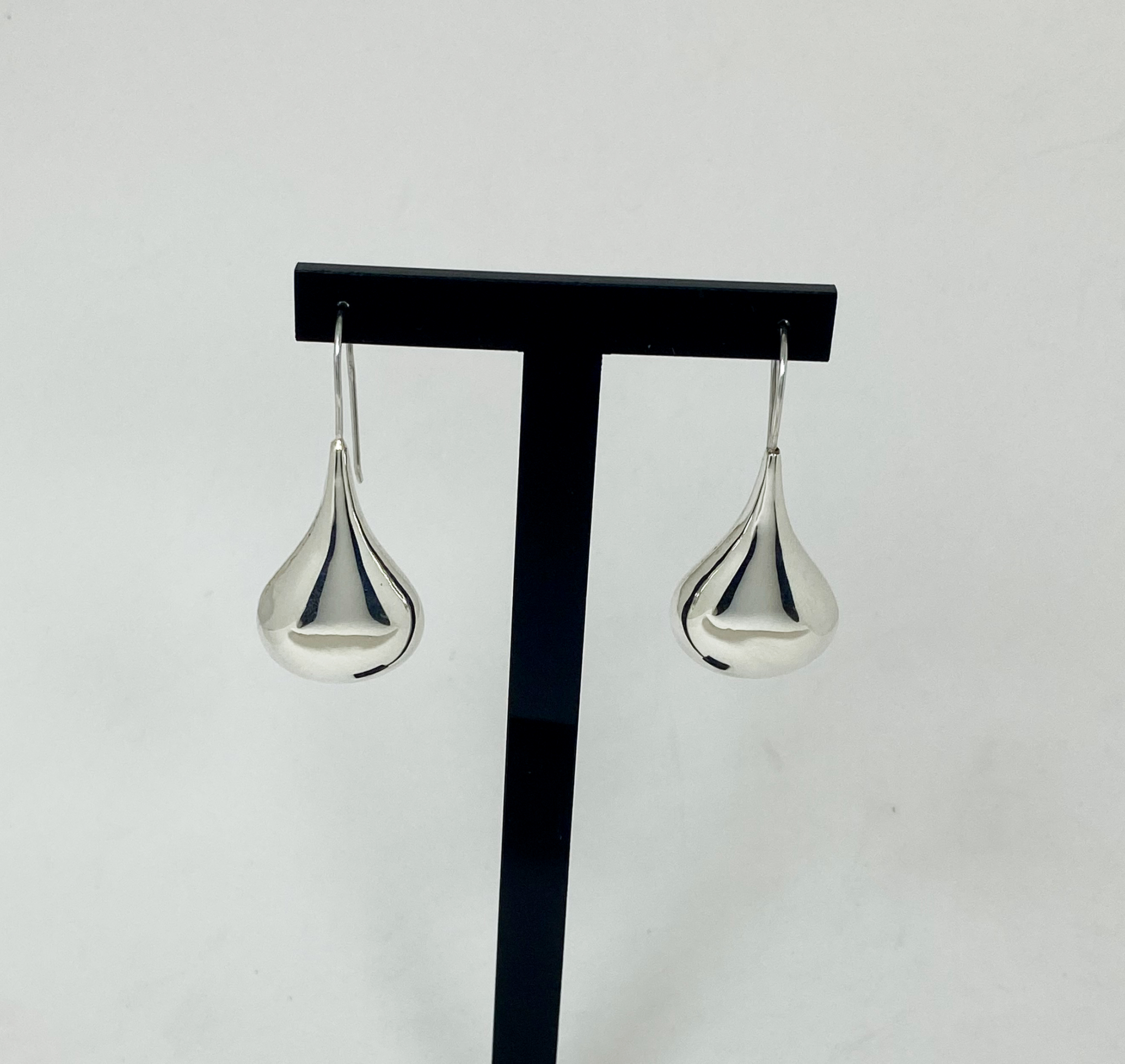 A pair of silver puffy teardrop earrings hanging from a T-shaped jewelry display stand.