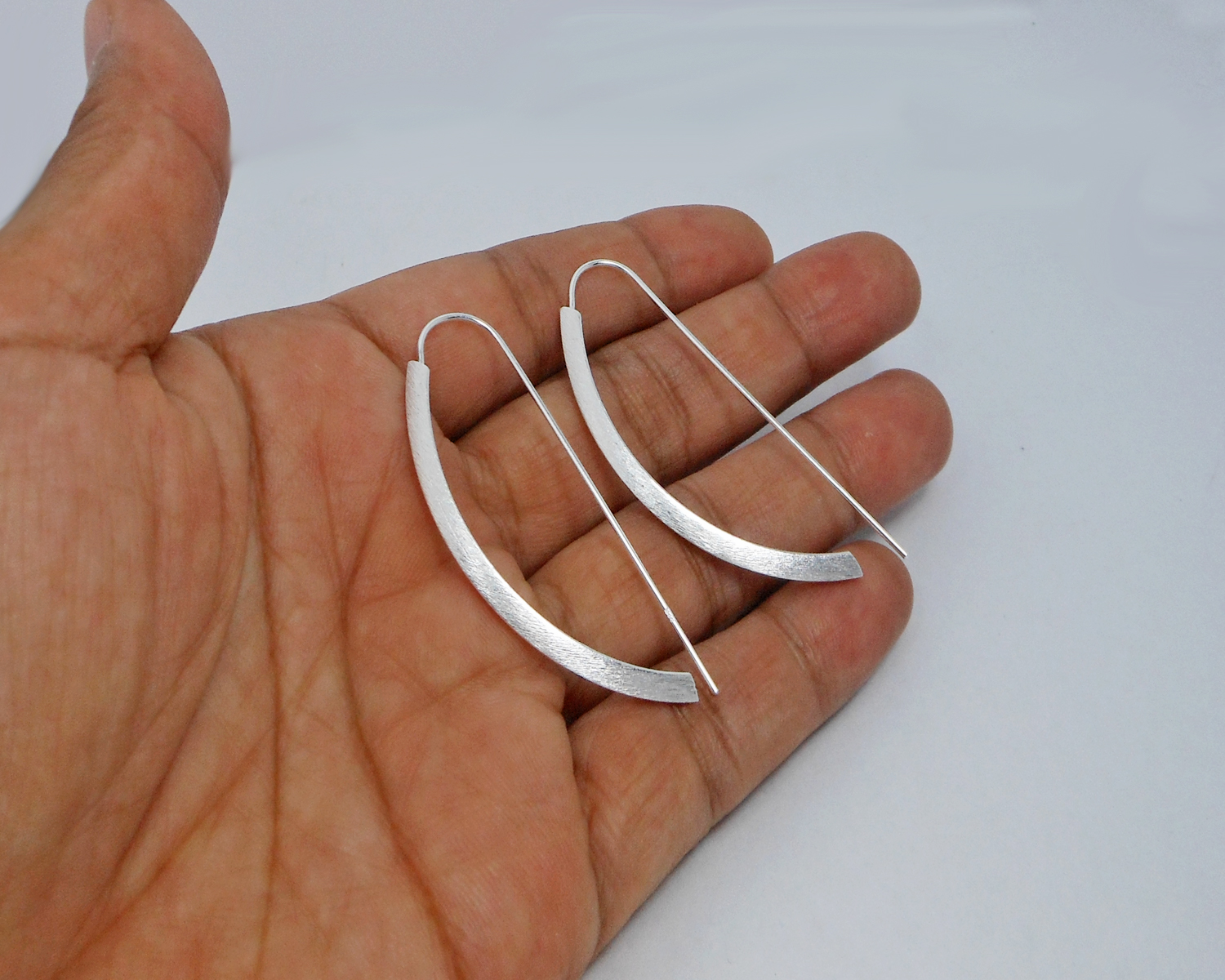 Pair of handmade 925 sterling silver arc D-hoop threader earrings held in a hand.