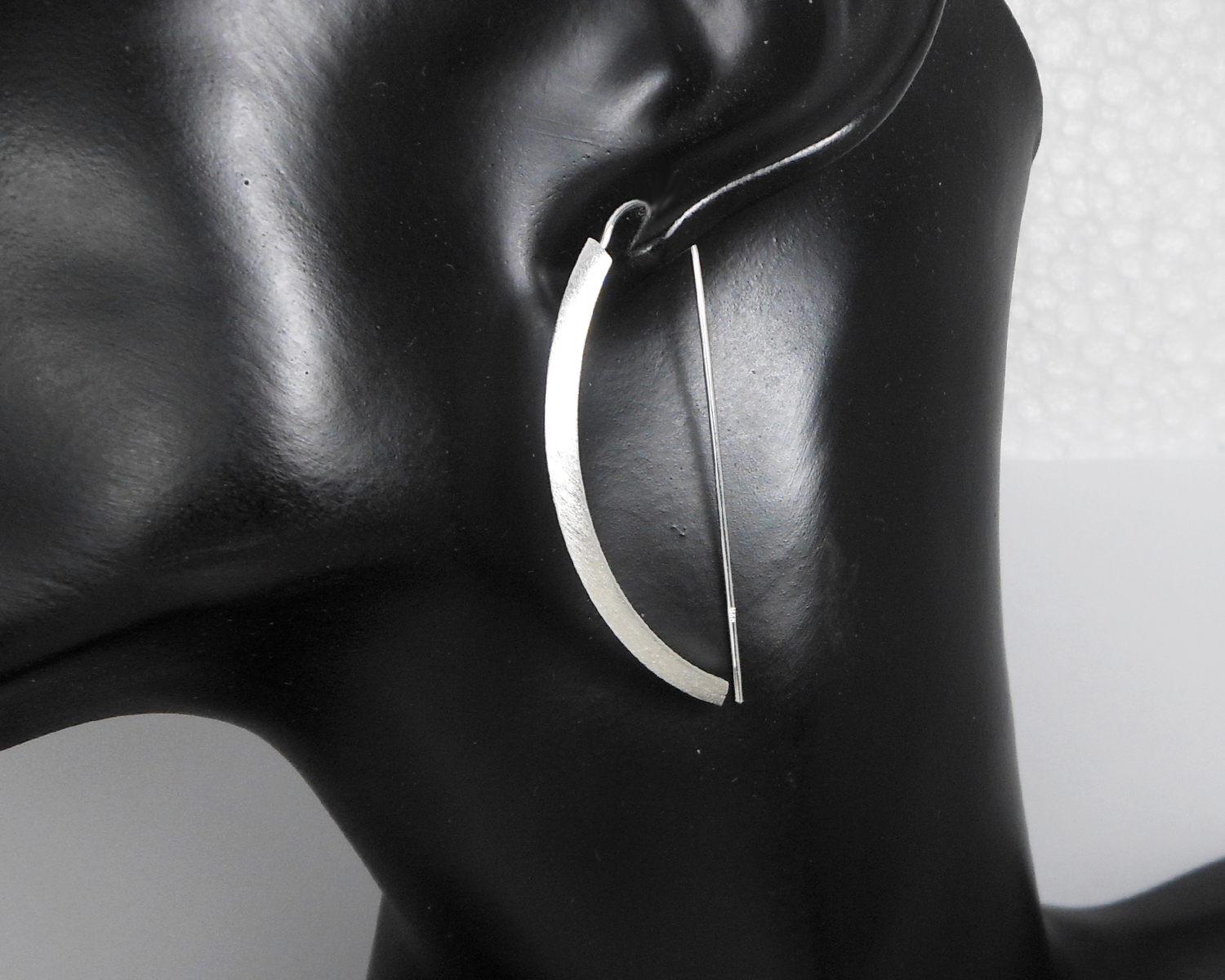 Close-up of silver arc D-hoop threader earrings on a black display stand.
